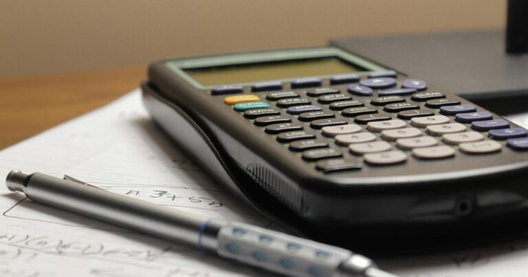 A notebook beside a calculator and stock charts, illustrating the Buffett-style focus on the boring investing habits behind strong decisions